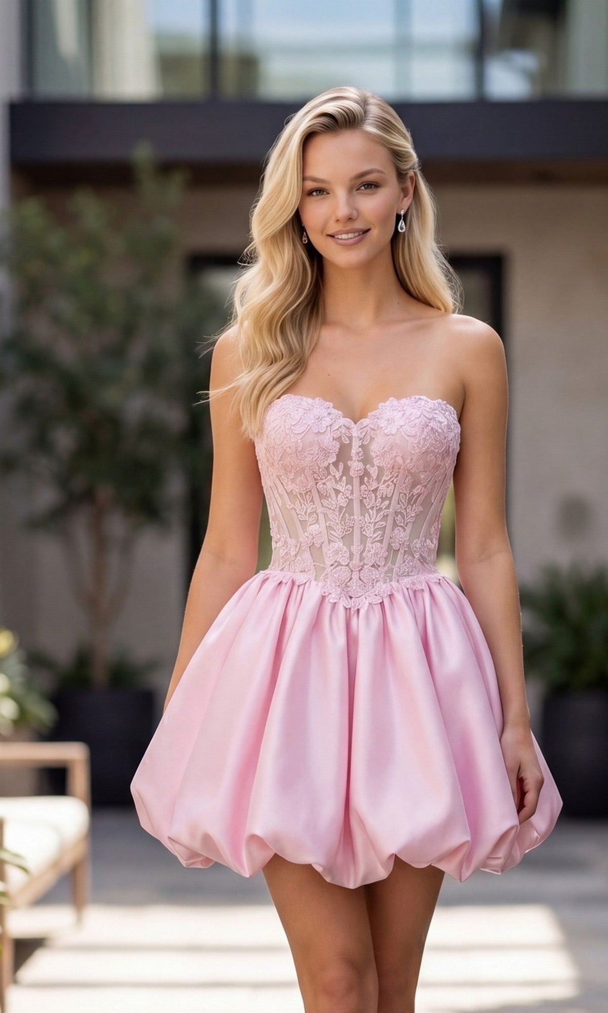 A woman stands outdoors in the Nox Anabel Q7122 short homecoming dress in baby pink, featuring a strapless lace corset bodice and a bubble-hem skirt.
